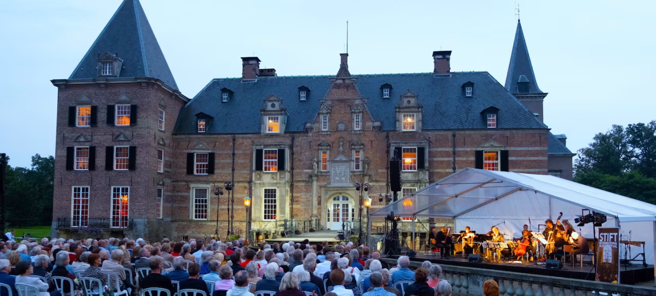 Buitenconcert bij kasteel Twickel tijdens Stiftfestival met orkest en publiek in schemerlicht