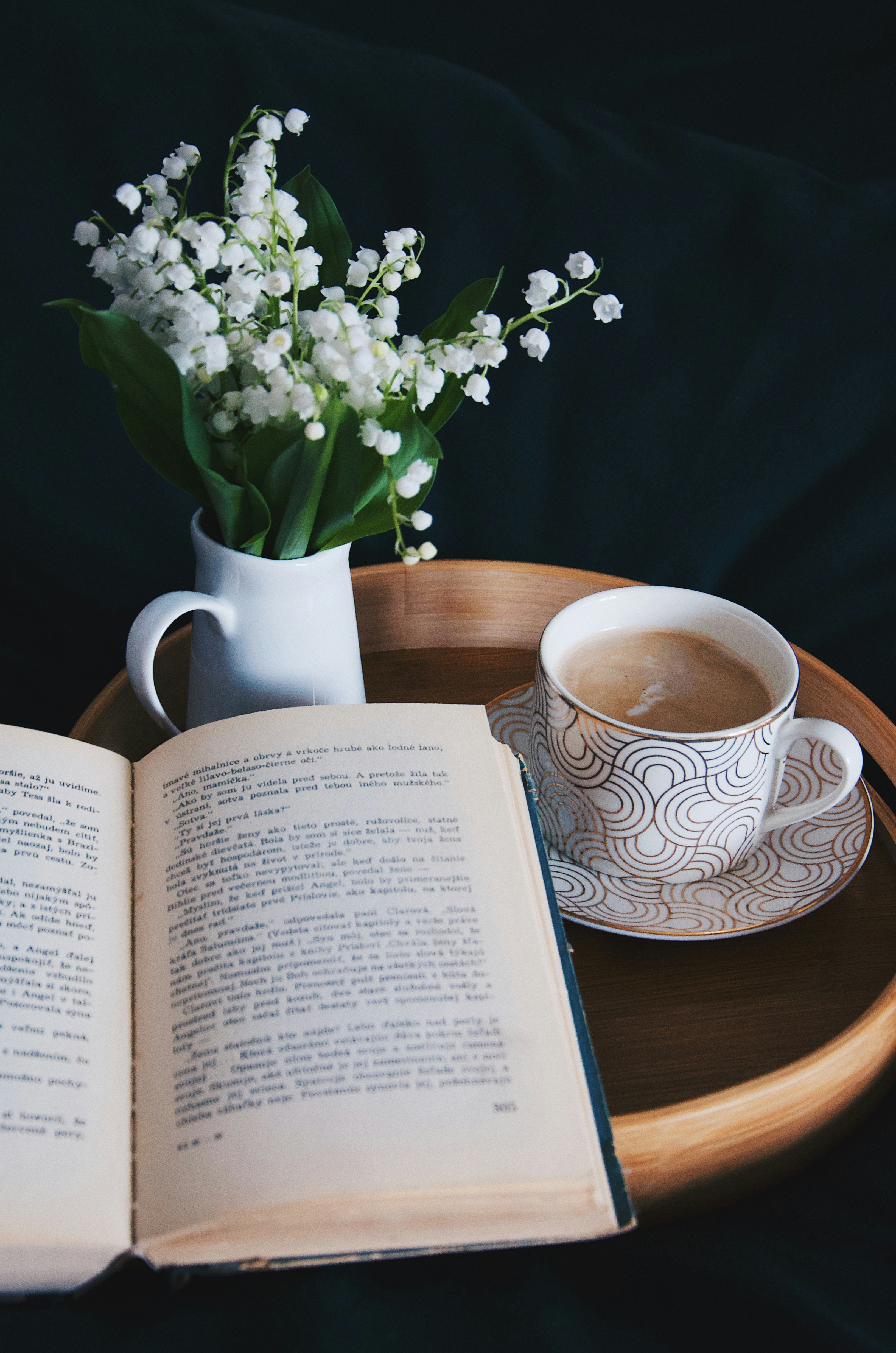 Onderweg naar plagwijk houten dienblad met open boek en bloemen lelietjes-van-dalen en koffie cup sfeervol stilleven
