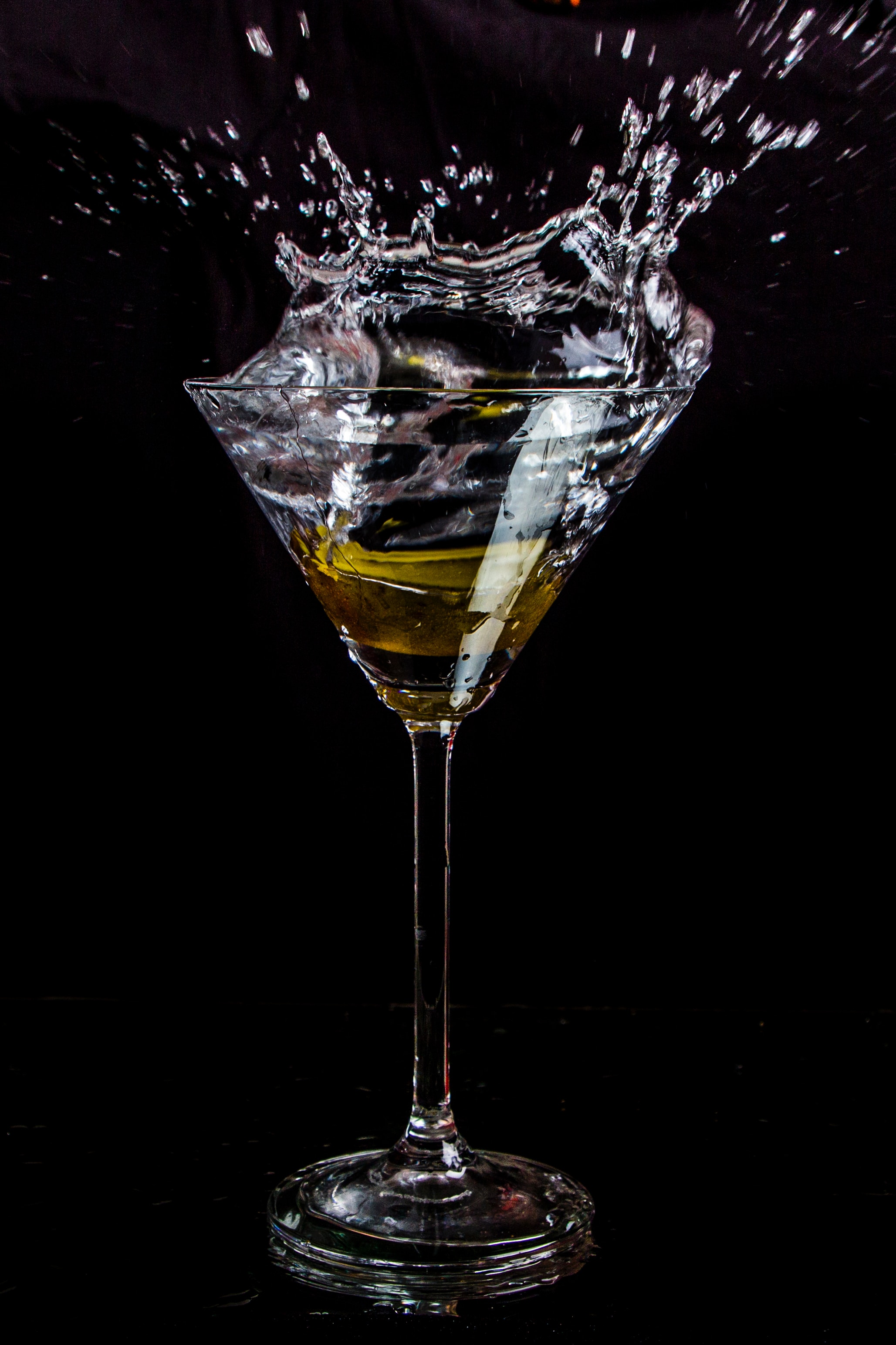 Cocktailglas met gele vloeistof en waterplons tegen zwarte achtergrond dry january actie en elegantie